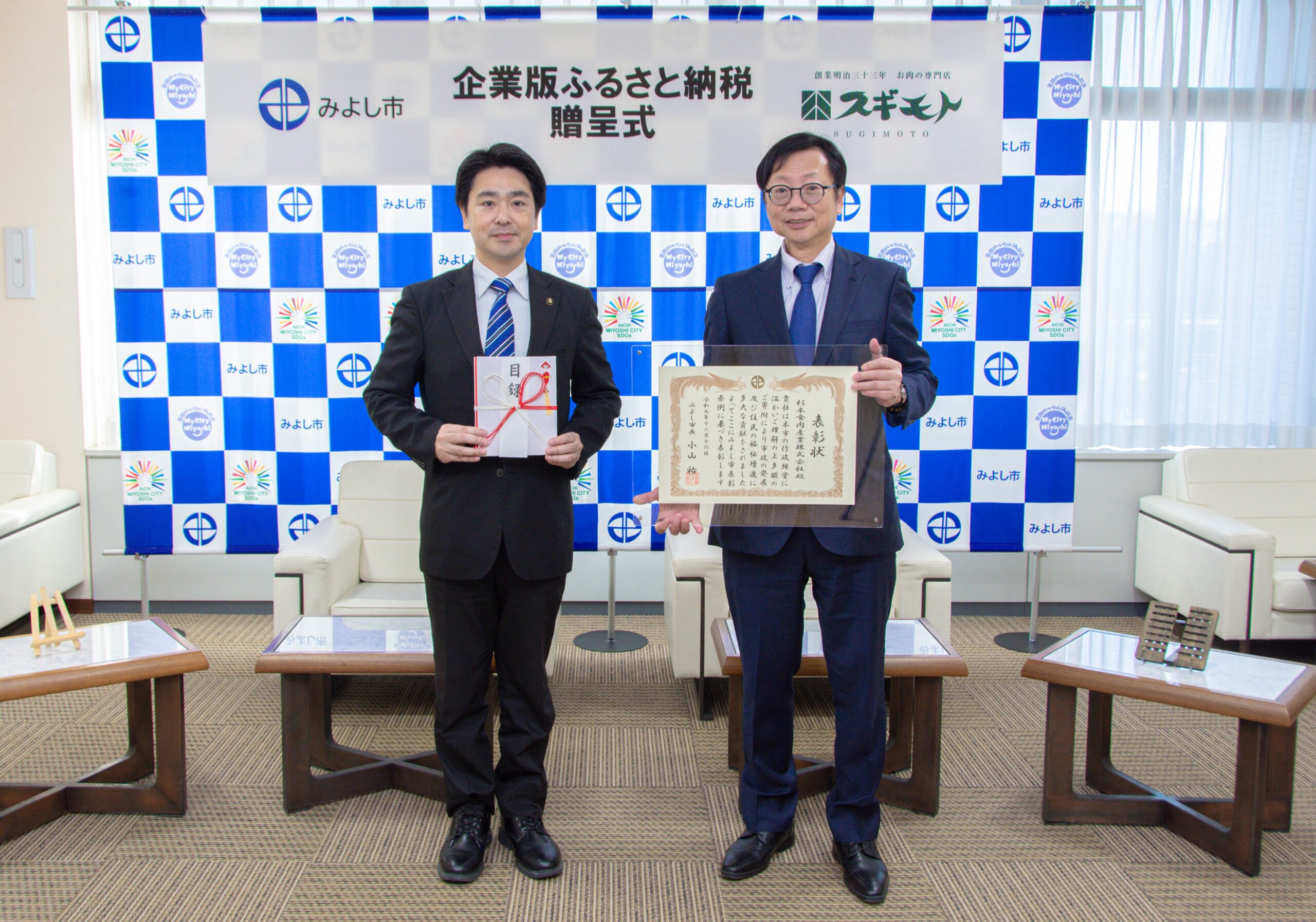 みよし市の市役所の部屋にて、二人の男性が表彰状を持って立っている。左はみよし市の小山市長、右は杉本食肉産業株式会社代表取締役の杉本達哉。